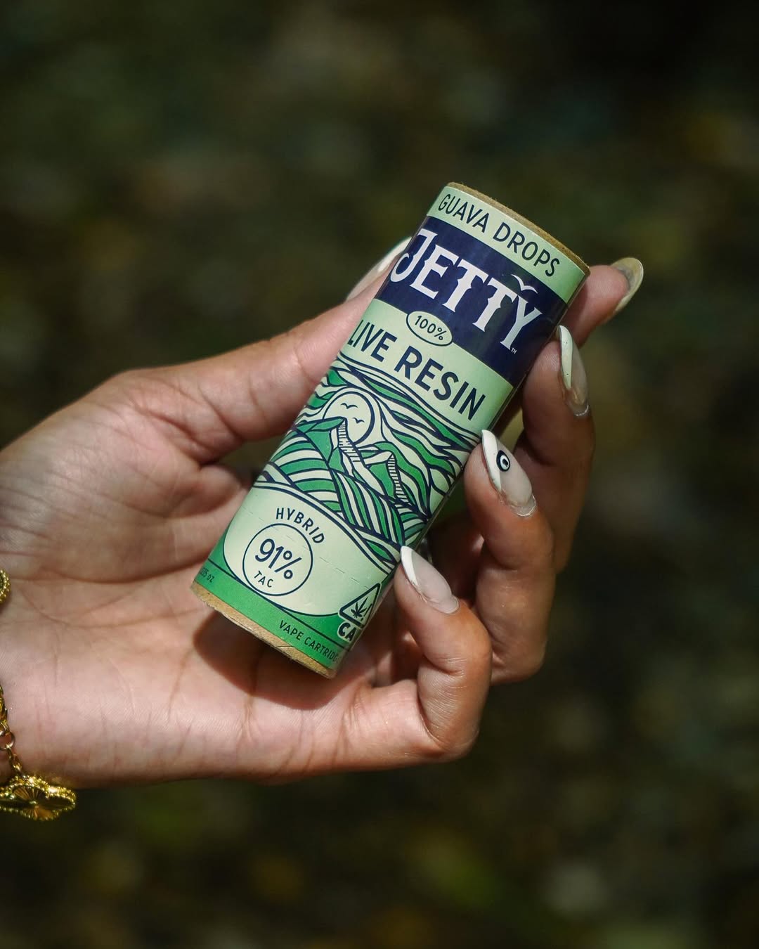 Hand with long nails holding a Jetty Guava Drops live resin vape cartridge tube outdoors